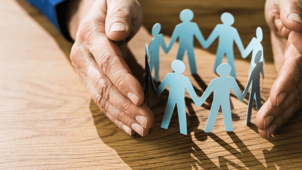 An elderly person's hands lightly wrap around a chain of paper figures in the shape of people. It represents adult safeguarding.
