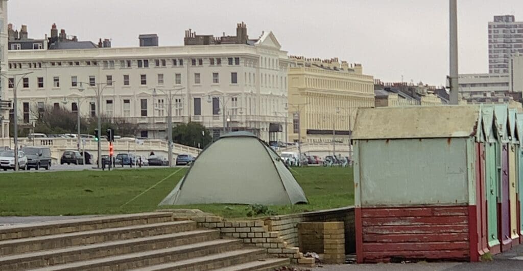 Green tent on city seafront near beach huts. - Supported housing crisis