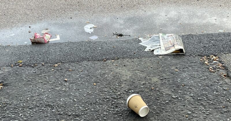 Litter scattered on wet pavement, cup and papers.
