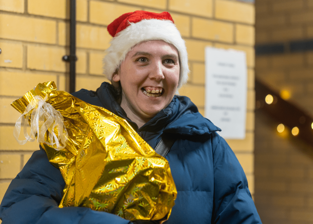 Person in Santa hat holding golden wrapped gift
